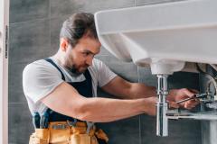 focused-male-plumber-in-working-overall-fixing-sink-in-bathroom